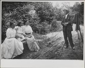 [Photographer with tripod set up to take a portrait of two women and a girl]