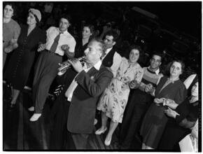 [Man playing a pipe as people dance.]