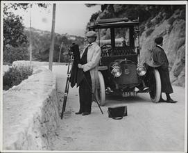[Photographer setting up his camera in front of an automobile]