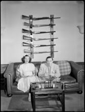 Billy Rose [Billy Rose and Eleanor Holm sitting on a couch in front of a gun rack.]