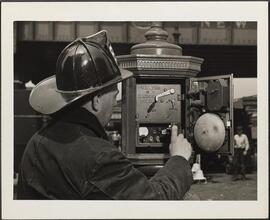[Fire fighter with fire alarm box.]