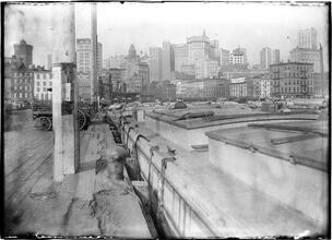"New Amsterdam Today", view of the Battery [canal barges in the foreground, tall buildings behind]