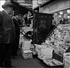 Newsstand [People browsing through magazine racks at a busy sidewalk newsstand.]