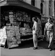 Newsstand [People browsing through magazine racks at a busy sidewalk newsstand.]