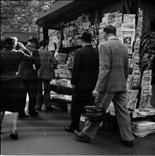 Newsstand [People browsing through magazine racks at a busy sidewalk newsstand.]