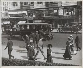 [Street scene with shops, pedestrians, cars, and a horse cart.]