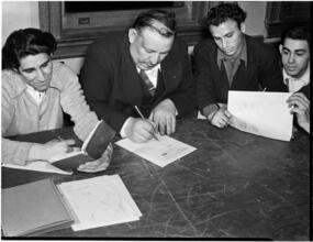[Men reading and writing at a table.]
