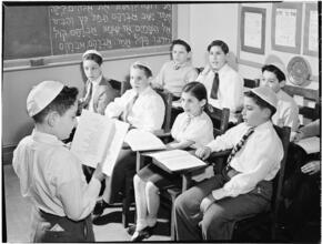 [Boy reading aloud in front of a classroom.]