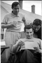 Leonard Bernstein [Leonard Bernstein looking at photographs as two men look over his shoulder.]