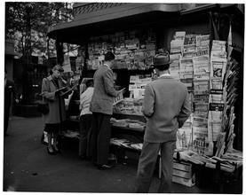 Newsstand [People browsing through magazine racks at a busy sidewalk newsstand.]