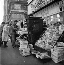 Newsstand [People browsing through magazine racks at a busy sidewalk newsstand.]