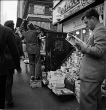 Newsstand [People browsing through magazine racks at a busy sidewalk newsstand.]