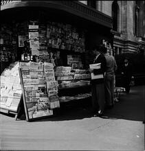 Newsstand [People browsing through magazine racks at a busy sidewalk newsstand.]