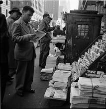 Newsstand [People browsing through magazine racks at a busy sidewalk newsstand.]