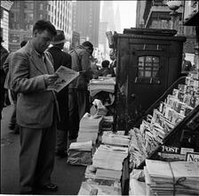 Newsstand [People browsing through magazine racks at a busy sidewalk newsstand.]