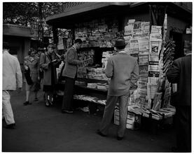 Newsstand [People browsing through magazine racks at a busy sidewalk newsstand.]