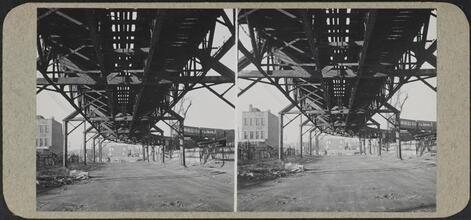 Elevated train tracks over dirt road.