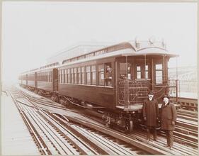 [Men standing next to elevated train.]