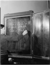 [Boy writing on a chalkboard.]