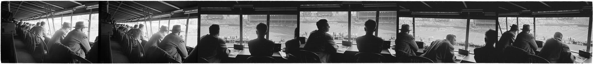 Football Writers [Reporters commentating on a football game in a stadium from the press box.]
