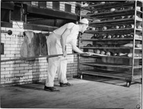 [Man putting loaves of bread on cooling racks.]
