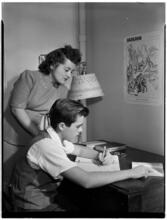 [Woman watching a boy study.]