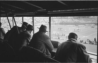 Football Writers [Reporters commentating on a football game in a stadium from the press box.]