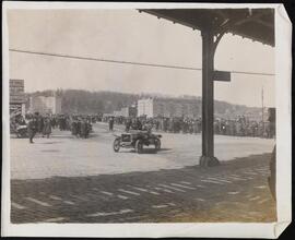 [Car and crowds under El train tracks.]