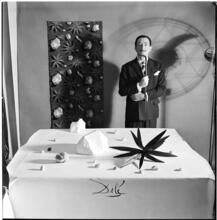 Salvador Dali: Rugs [Salvador Dali standing in front of a rug he designed near a table with objects.]