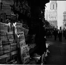 Newsstand [People browsing through magazine racks at a busy sidewalk newsstand.]