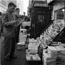 Newsstand [People browsing through magazine racks at a busy sidewalk newsstand.]