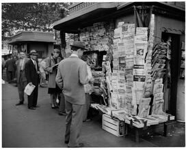 Newsstand [People browsing through magazine racks at a busy sidewalk newsstand.]