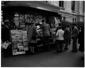 Newsstand [People browsing through magazine racks at a busy sidewalk newsstand.]