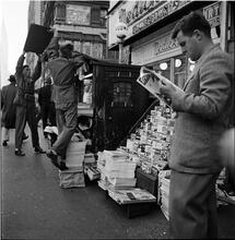 Newsstand [People browsing through magazine racks at a busy sidewalk newsstand.]