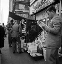 Newsstand [People browsing through magazine racks at a busy sidewalk newsstand.]