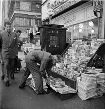 Newsstand [People browsing through magazine racks at a busy sidewalk newsstand.]