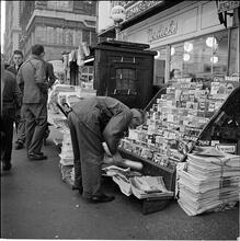 Newsstand [People browsing through magazine racks at a busy sidewalk newsstand.]