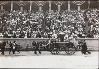 [Firemen pulling fire engine in front of a crowd.]