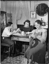 [Women sewing with boy reading.]