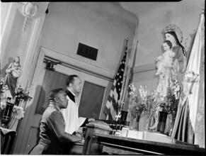 [Men praying before a statue of Madonna and Child.]