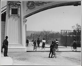 [Bicyclists passing under wooden arch at the opening of Grant's Tomb]