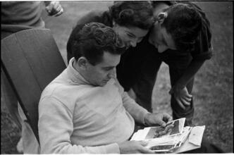 Leonard Bernstein [Leonard Bernstein looking at photographs as two people look over his shoulder.]