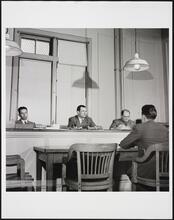 [Man meeting with officials on Ellis Island.]