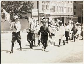 [Children marching in parade with American Flags.]