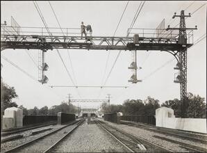 [Photographer standing on superstructure above train tracks]