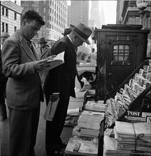 Newsstand [People browsing through magazine racks at a busy sidewalk newsstand.]