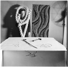Salvador Dali: Rugs [Salvador Dali standing in front of a rug he designed near a table with objects.]