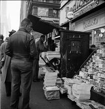 Newsstand [People browsing through magazine racks at a busy sidewalk newsstand.]