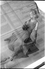 [Mannequin in window display, with buildings reflected in window.]