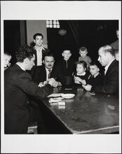 [People playing a card game while children watch at Ellis Island.]